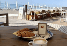 A cappuccino and croissants on a table overlooking the beach with umbrellas and the sea in Eraclea Mare, Italy.