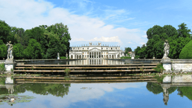 A front view of the grand Villa Pisani in Italy, with its symmetrical reflection in the calm water in the foreground.