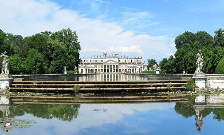 A front view of the grand Villa Pisani in Italy, with its symmetrical reflection in the calm water in the foreground.